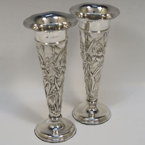 A very pretty Antique Edwardian Sterling Silver pair of table flower vases, having round hand-chased bodies with tapering sides and floral decoration, and all sitting on pedestal feet. These beautiful antique silver vases were made by William Comyns of London in 1903. The dimensions of these fine hand-made antique silver pair of vases are height 16.5 cms (6.5 inches), and diameter at top 7 cms (2.75 inches).   