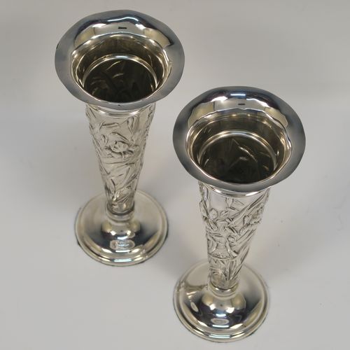 A very pretty Antique Edwardian Sterling Silver pair of table flower vases, having round hand-chased bodies with tapering sides and floral decoration, and all sitting on pedestal feet. These beautiful antique silver vases were made by William Comyns of London in 1903. The dimensions of these fine hand-made antique silver pair of vases are height 16.5 cms (6.5 inches), and diameter at top 7 cms (2.75 inches).   