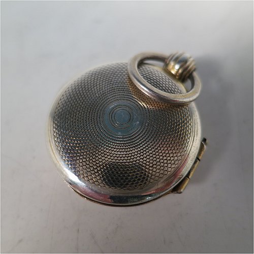 An Antique Georgian Sterling Silver vinaigrette, having a round body in the shape of a fob watch, with engine-turned decoration on the top and base, a hinged lid with ring for a chain, and a gold-gilt interior with a plain hand-pierced grill. Made by John Lawrence, of Birmingham in 1828. The dimensions of this fine hand-made antique silver vinaigrette are diameter length 2.5 cms (1 inch), and depth 0.8 cms (0.3 inches).   