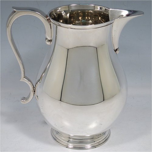 A Sterling Silver water jug, in a George I beer jug style, having a plain round bellied body, sparrow-beak spout, scroll handle, and sitting on a pedestal foot. Made by Robert Comyns of London in 1939. The dimensions of this fine hand-made silver water jug are height 17 cms (6.75 inches), length 16.5 cms (6.5 inches), length 16 cms (6.25 inches), and it weighs approx. 465g (15 troy ounces).