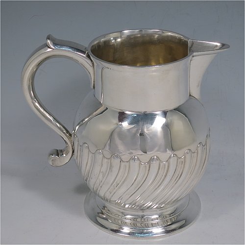 An Antique Georgian Sterling Silver water or beer jug, having a round bellied body with hand-chased swirl-fluted decoration, sparrow-beak spout, scroll handle, and sitting on a collet foot. Made by William Grundy of London in 1765. The dimensions of this fine hand-made antique silver water or beer jug are height 13.5 cms (5.3 inches), length 15 cms (6 inches), and it weighs approx. 372g (12 troy ounces).   