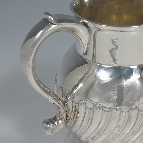 An Antique Georgian Sterling Silver water or beer jug, having a round bellied body with hand-chased swirl-fluted decoration, sparrow-beak spout, scroll handle, and sitting on a collet foot. Made by William Grundy of London in 1765. The dimensions of this fine hand-made antique silver water or beer jug are height 13.5 cms (5.3 inches), length 15 cms (6 inches), and it weighs approx. 372g (12 troy ounces).   