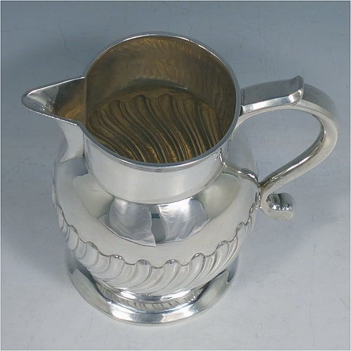 An Antique Georgian Sterling Silver water or beer jug, having a round bellied body with hand-chased swirl-fluted decoration, sparrow-beak spout, scroll handle, and sitting on a collet foot. Made by William Grundy of London in 1765. The dimensions of this fine hand-made antique silver water or beer jug are height 13.5 cms (5.3 inches), length 15 cms (6 inches), and it weighs approx. 372g (12 troy ounces).   