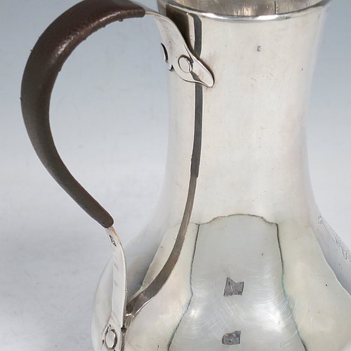 An Antique Georgian Sterling Silver George II very unwater jug, having a plain round bellied body, a sparrow-beak spout, a riveted scroll handle with leather cover, and sitting on a collet foot. Made by William Cripps (possibly) of London in 1755. The dimensions of this fine hand-made antique silver water jug are height 17 cms (6.75 inches), length 13 cms (5 inches), and it weighs approx. 250g (8 troy ounces). Please note that this item is crested.   