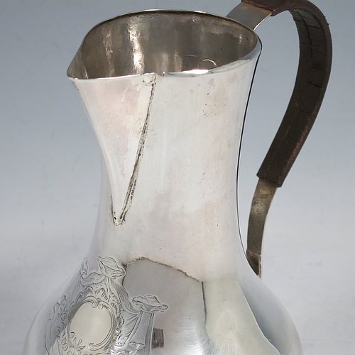 An Antique Georgian Sterling Silver George II very unwater jug, having a plain round bellied body, a sparrow-beak spout, a riveted scroll handle with leather cover, and sitting on a collet foot. Made by William Cripps (possibly) of London in 1755. The dimensions of this fine hand-made antique silver water jug are height 17 cms (6.75 inches), length 13 cms (5 inches), and it weighs approx. 250g (8 troy ounces). Please note that this item is crested.   