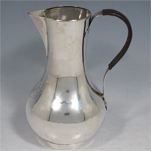 An Antique Georgian Sterling Silver George II very unwater jug, having a plain round bellied body, a sparrow-beak spout, a riveted scroll handle with leather cover, and sitting on a collet foot. Made by William Cripps (possibly) of London in 1755. The dimensions of this fine hand-made antique silver water jug are height 17 cms (6.75 inches), length 13 cms (5 inches), and it weighs approx. 250g (8 troy ounces). Please note that this item is crested.   