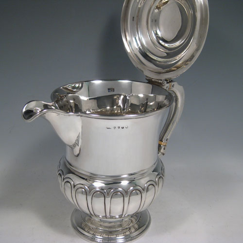 A large and very handsome Antique Georgian Sterling Silver water or beer jug, having a round body with hand-chased half-fluted decoration, plain pouring spout, an insulated scroll handle, a hinged domed lid with cast acanthus leaf thumb-piece, and sitting on a plain round pedestal foot. Made by J. McKay of Edinburgh in 1811. The dimensions of this fine hand-made antique silver beer or water jug are height 23 cms (9 inches), length 26 cms (10.25 inches), and it weighs approx. 991g (32 troy ounces)