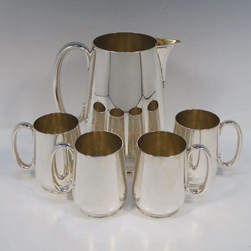 A very handsome Antique Edwardian Silver-Plated  water jug with four mugs, in a very plain style, having round bellied bodies with tapering sides, a sparrow-beak spout, scroll side-handles, gold-gilt interiors, and all sitting on collet feet. This antique silver-plated water jug serving set was made in ca. 1900 by Martin Hall and Co., of Sheffield. The dimensions of this fine hand-made silver-plated water jug are height 20 cms (8 inches), and height of mugs are 10 cms (4 inches).   