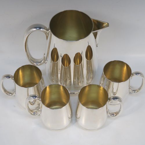 A very handsome Antique Edwardian Silver-Plated  water jug with four mugs, in a very plain style, having round bellied bodies with tapering sides, a sparrow-beak spout, scroll side-handles, gold-gilt interiors, and all sitting on collet feet. This antique silver-plated water jug serving set was made in ca. 1900 by Martin Hall and Co., of Sheffield. The dimensions of this fine hand-made silver-plated water jug are height 20 cms (8 inches), and height of mugs are 10 cms (4 inches).   