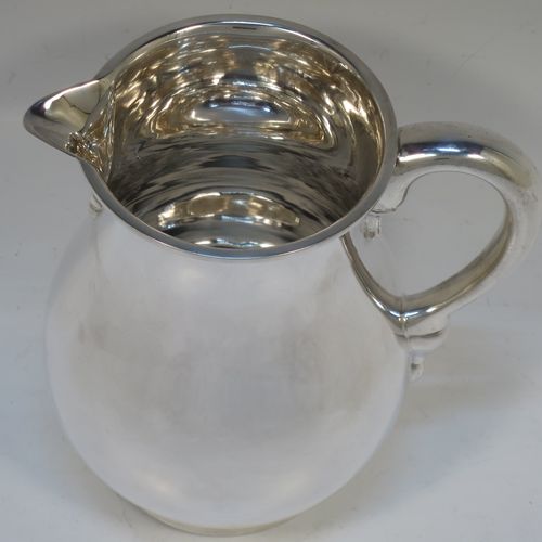 A very handsome American Sterling Silver water jug, in a George I beer jug style, having a plain round bellied body, sparrow-beak spout, a scroll handle, and sitting on a collet foot. Made in ca. 1930 in North America. The dimensions of this fine hand-made silver water jug are height 16.5 cms (6.5 inches), length 16 cms (6.25 inches), and it weighs approx. 512g (16.5 troy ounces).   