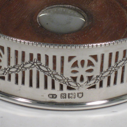 Sterling silver pair of wine bottle table coasters, having round bodies with hand-pierced decoration and engraved swags, with wood-turned bases and silver buttons, and applied beaded borders. Made by Henry Freeman Ltd., of London in 1913. The dimensions of these wine coasters are diameter 13 cms (5 inches), height 4 cms (1.5 inches).   