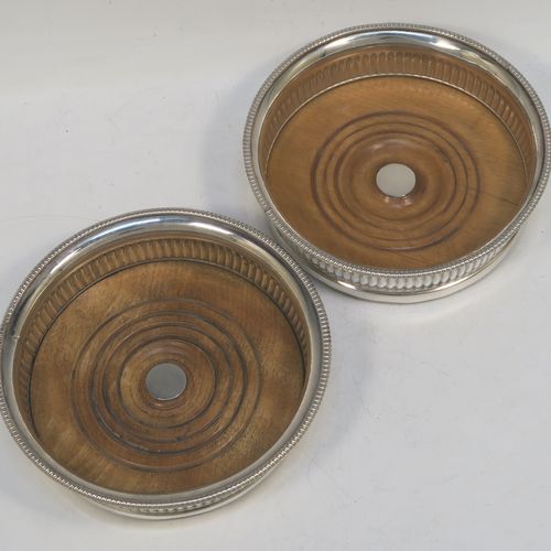 A very handsome Antique Georgian Old Sheffield plated pair of table wine coasters, in a Regency style, having round bellied bodies, with applied gadroon borders, and hand-chased fluted decoration, and with wood-turned bases and silver buttons. Made in ca. 1810. The dimensions of this fine pair of antique hand-made Old Sheffield plated wine bottle coasters are diameter 14 cms (5.5 inches), and height 4 cms (1.5 inches).   