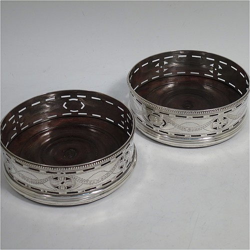 A very pretty Antique Georgian Sterling Silver pair of Neoclassical style wine coasters, having hand-pierced walls with hand-engraved neoclassical decoration, applied bead-edge borders, and oak hand-turned bases. Made by Benjamin Mountigue of London in 1786. The dimensions of this fine hand-made antique pair of neoclassical style silver wine bottle coasters are diameter 11.5 cms (4.5 inches), and height 4 cms (1.5 inches).