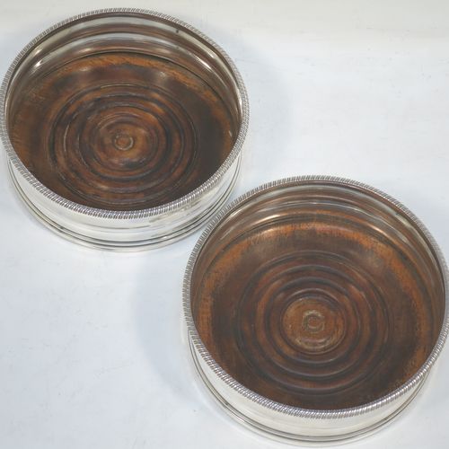 A very elegant pair of Antique Georgian Sterling Silver table wine bottle coasters, having plain round double bellied bodies, with applied gadroon or rope-twist borders, and oak wood turned bases. Made by James Barratt of London in 1812. The dimensions of these fine hand-made antique silver wine bottle coasters are diameter 13 cms (3.25 inches), and height 5 cms (2 inches).   