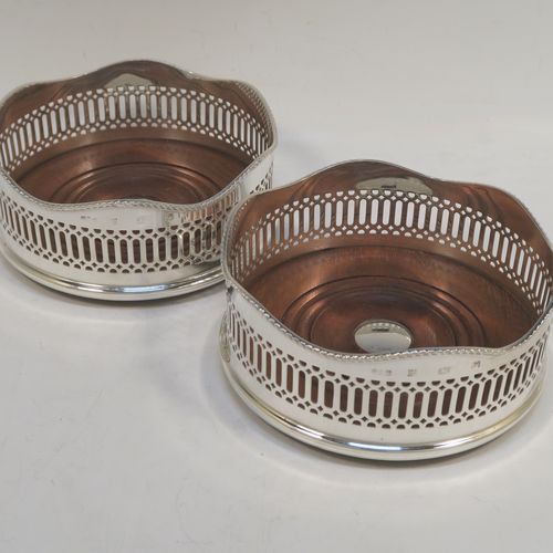 A large and very elegant Sterling Silver pair of Neoclassical style wine coasters, having hand-pierced walls with  applied wavy gadroon-edged borders, and plain oak-turned bases with silver buttons. These beautiful silver bottle coasters were made by R. E. Porter of Birmingham in 1989. The dimensions of this fine hand-made pair of silver wine bottle coasters are diameter 14 cms (5.5 inches), and height 5.5 cms (2.25 inches).   