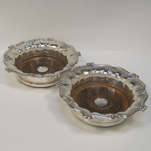 A very handsome Antique Georgian Old Sheffield plated pair of table wine coasters, having round bodies with melon fluted sides, applied floral and scroll borders, and wood-turned bases with silver buttons. These elegant antique wine bottle coasters were made in ca. 1830. The dimensions of this fine hand-made pair of antique Old Sheffield silver plated wine coasters are diameter 18 cms (7 inches), and height 5 cms (2 inches).  