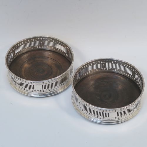 A very handsome Antique Georgian Old Sheffield Plated pair of Neoclassical style wine coasters, having hand-pierced walls, applied bead-edged borders, and plain oak-turned bases. These beautiful antique silver-plated bottle coasters were made in ca. 1780. The dimensions of this fine hand-made antique pair of Old Sheffield Plated silver wine bottle coasters are diameter 13 cms (5.25 inches), and height 4.5 cms (1.75 inches).    