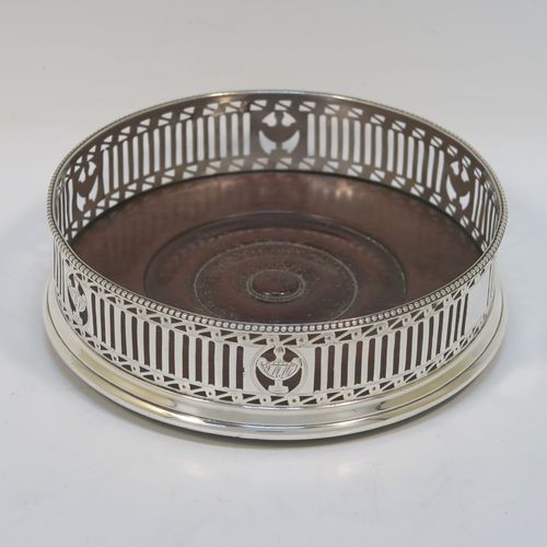 A very pretty Antique Georgian Neoclassical style Sterling Silver wine bottle table coaster, having a round hand-pierced body with geometrical and tureen style decoration, together with an applied bead-edged top border, and an wood-turned base. This beautiful antique silver wine bottle coaster was made in London in 1786. The dimensions of this fine hand-made antique silver wine bottle coaster are diameter 12 cms (4.75 inches), and height 3.5 cms (1.3 inches).   