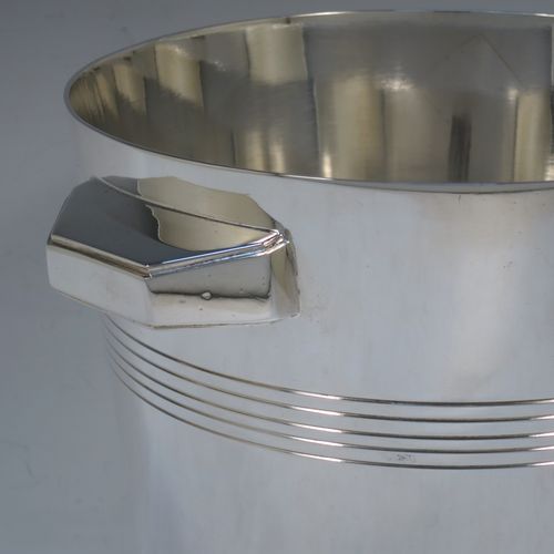 A very handsome Art Deco style Silver Plated wine bottle cooler, having a plain round body with tapering sides, with two cast angular side-handles, and two bands of hand-chased reeded decoration, all sitting on a flat base. Made in ca. 1930. The dimensions of this fine hand-made silver-plated  wine cooler are height 21 cms (8.25 inches), and diameter at lip 18.5 cms (7.25 inches). Please note that this will easily hold a magnum size bottle.