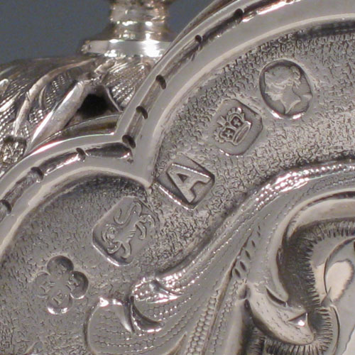 Antique Victorian sterling silver wine ewer, having a round body with hand-chased floral work, swirl fluting, and oval panels with a vacant cartouche, with a hinged lid and pineapple finial attached to a foliate mechanised handle, and all sitting on a pedestal foot with bead border. Made by Martin and Hall of Sheffield in 1868. Height 32 cms (12.5 inches), length 16.5 cms (6.5 inches). Weight approx. 982g (31.7 troy ounces).