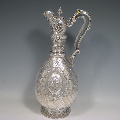 Antique Victorian sterling silver wine ewer, having a round body with hand-chased floral work, swirl fluting, and oval panels with a vacant cartouche, with a hinged lid and pineapple finial attached to a foliate mechanised handle, and all sitting on a pedestal foot with bead border. Made by Martin and Hall of Sheffield in 1868. Height 32 cms (12.5 inches), length 16.5 cms (6.5 inches). Weight approx. 982g (31.7 troy ounces).