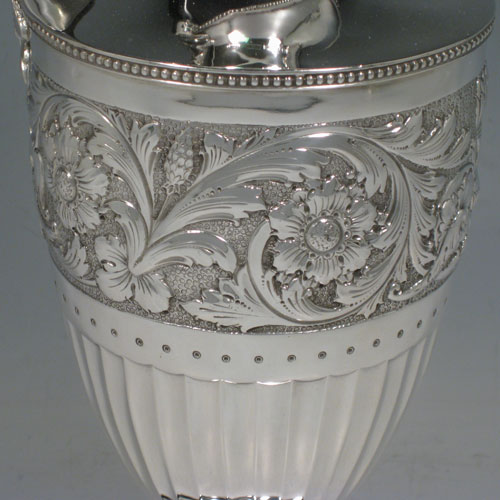 Antique Victorian sterling silver pair of Neoclassical style wine ewers, having round bodies with tapering sides, all hand-chased with floral bands and half-fluting, wooden scroll handles, hinged lids with wooden finials, applied bead-edged borders, and all sitting on pedestal feet. Made by William Hutton of London in 1896 and 1899. The dimensions of these fine hand-made silver wine ewers are height 32 cms (12.5 inches), length 15 cms (6 inches), and they weigh a total of 1,085g (35 troy ounces). Please note that because these ewers were made within three years of each other the body of the 1896 ewer is slightly larger in diameter.   