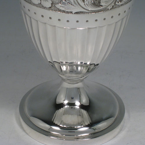 Antique Victorian sterling silver pair of Neoclassical style wine ewers, having round bodies with tapering sides, all hand-chased with floral bands and half-fluting, wooden scroll handles, hinged lids with wooden finials, applied bead-edged borders, and all sitting on pedestal feet. Made by William Hutton of London in 1896 and 1899. The dimensions of these fine hand-made silver wine ewers are height 32 cms (12.5 inches), length 15 cms (6 inches), and they weigh a total of 1,085g (35 troy ounces). Please note that because these ewers were made within three years of each other the body of the 1896 ewer is slightly larger in diameter.   