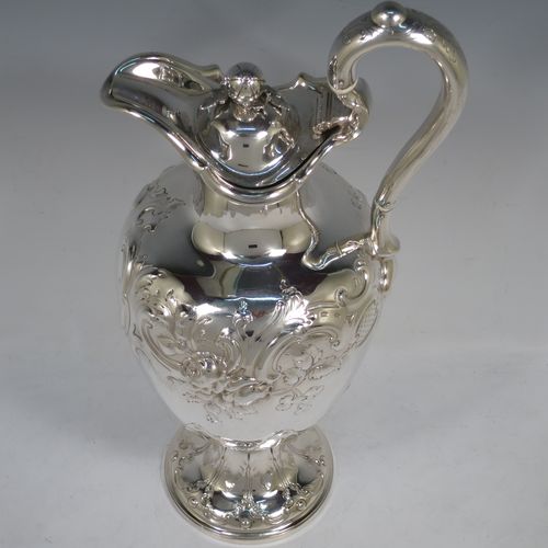 A beautiful Antique Victorian Sterling Silver wine ewer, having an amphora style round bellied body, with hand-chased floral and scroll decoration, a hinged lid with cast finial, an insulated scroll handle, and all sitting on a pedestal foot. This handsome antique silver ewer was made by the Barnard Brothers of London in 1849. The dimensions of this fine hand-made antique silver wine ewer are height 35 cms (13.5 inches), length 16.5 cms (6.5 inches), and it weighs approx. 868g (28 troy ounces).    