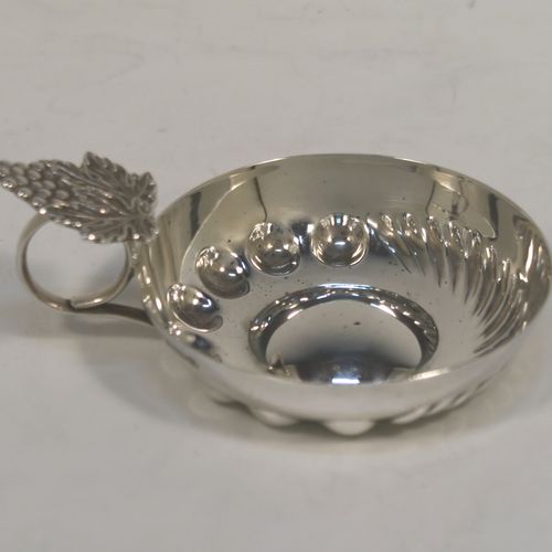 A very pretty Sterling Silver testavine or wine taster, having a round body, with hand-chased bead and swirl-fluted decoration, a loop handle with a cast grape and vine thumb-piece, and all sitting on a concave base. This handsome silver wine taster or testavine was made by A. E. Jones of Birmingham in 1979. The dimensions of this fine hand-made silver wine taster or testavine are diameter 8 cms (3 inches), and height 4 cms (1.5 inch), and it weighs approx. 62g (2 troy ounces).   